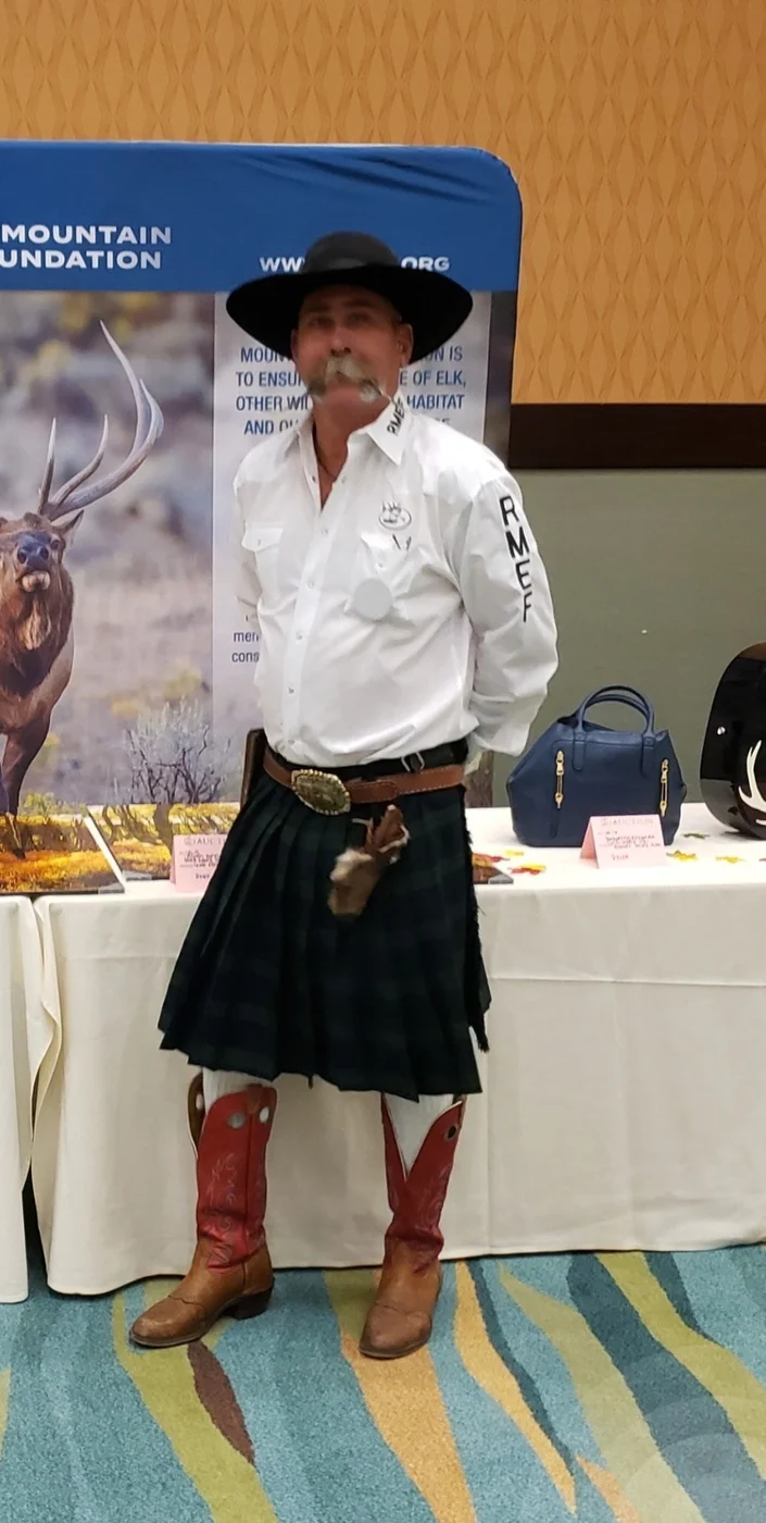 Kevin wearing a black cowboy hat, white shirt, kilt, and Western boots