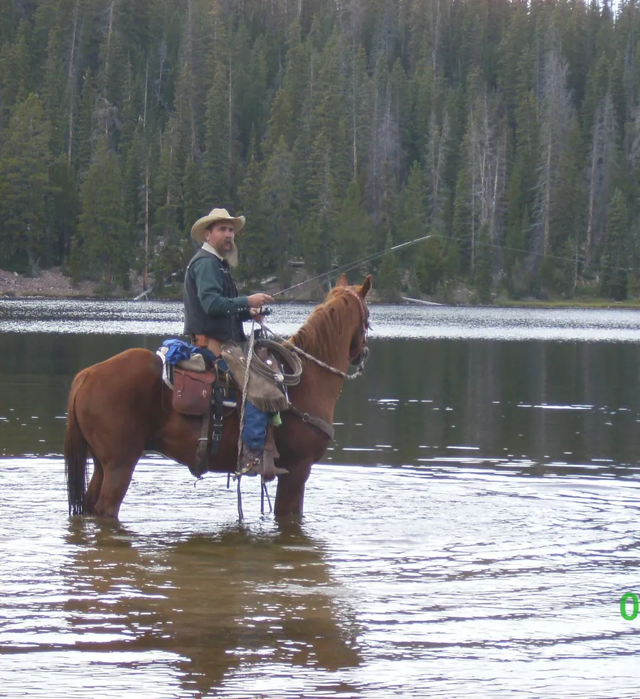 Kevin fishing from horseback in a lake surrounded by forest