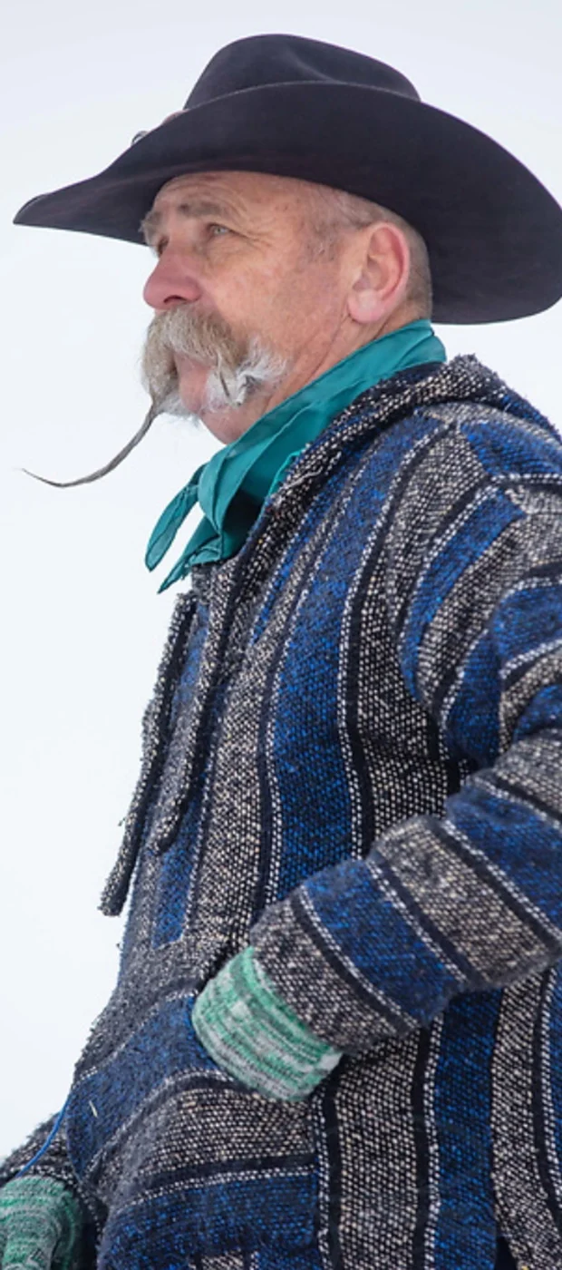 Kevin in a black cowboy hat, turquoise scarf, and blue patterned coat